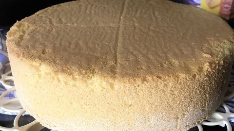 Ein goldfarbener Tortenboden steht auf einem weißen Gitter, bereit zum Dekorieren in einer dunklen Küchenszene.