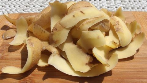 Frittierfett reinigen zum Wiederverwenden. Eine Holzbretter-Oberfläche zeigt frische Kartoffelschalen, die zum Frittieren verwendet werden können.