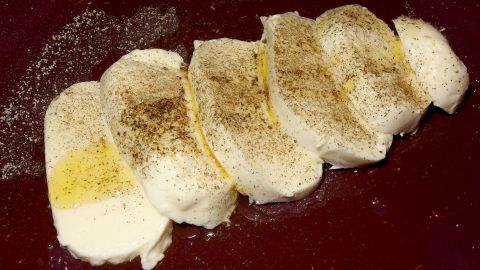 Scheiben von Mozzarella liegen auf einem dunklen Teller, gewürzt mit Pfeffer und einem Hauch von Öl, bereit zum Servieren.