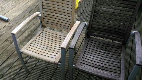 Zwei Holzgartenmöbel stehen nebeneinander, eines ist sauber und das andere schmutzig, auf einem Holzdeck.