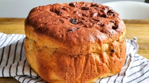 Ein frisch gebackener Panettone ruht auf einem gestreiften Küchentuch, umgeben von einer Holzoberfläche.