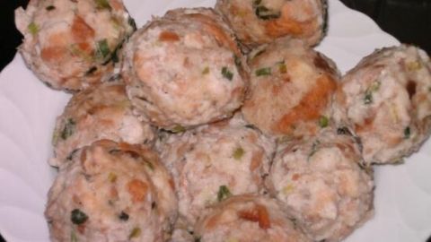 Semmelknödel sitzen auf einem weißen Teller, sind goldbraun mit Kräutern gesprenkelt und wirken appetitlich serviert.