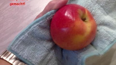 Ein Hand hält einen roten Apfel, der in ein Mikrofasertuch eingewickelt ist. Das Tuch wird verwendet, um Wachsschicht zu entfernen.