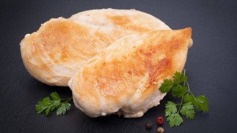 Saftige Hähnchenbrustfilets liegen gegrillt auf einer dunklen Platte, umgeben von frischen Kräutern und Gewürzen.
