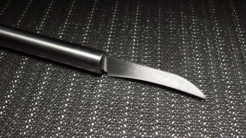 Ein Messer liegt auf einer strukturierten Oberfläche und zeigt eine geschwungene Klinge, bereit zum Schärfen mit einem Ledergürtel.