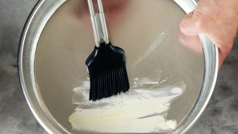 Eine Hand hält einen Pinsel, der Butterschmalz auf eine Backform verteilt, um sie einzufetten und Backergebnisse zu verbessern.