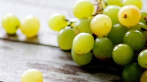 Eine Traube liegt neben einem Bündel saftiger, grüner Trauben auf einer rustikalen Holztischoberfläche.