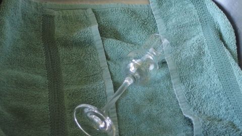 Ein empfindliches Glas liegt auf einem grünen Frotteetuch in der Spüle, bereit zum sicheren Spülen per Hand.