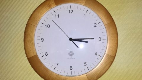 Holzuhr zeigt 10:10 an, hängt an beige Wand. Text: "RADIO CONTROLLED German Technology".