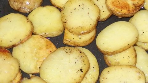 So schneidest Du Kartoffeln schnell und gleichmäßig: Nutze die Technik des Stapelns für perfekte Scheiben, um ein gleichmäßiges Garen und eine schöne Optik zu erreichen, wie im Bild gezeigt. Ideal für deine kulinarischen Kreationen. Kartoffelscheiben liegen goldbraun auf einer Pfanne, gleichmäßig geschnitten und mit Pfeffer gewürzt.