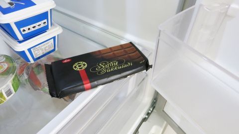 Größere Mengen Schokolade mit im Eisfach vorgekühlter Raffelscheibe der Küchenmaschine reiben, ebenso die Schokolade vorher kühlen. Eine Schokoladentafel liegt in einem Kühlschrank, bereit zum Raspeln mit der Küchenmaschine für ein Rezept.