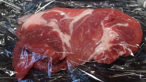 Zwei Stücke Schnitzel sind sorgfältig in Frischhaltefolie eingewickelt und liegen auf einem dunklen Untergrund.