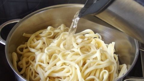 In einem Topf mit gekochten Spaghetti wird heißes Wasser eingefüllt, um sie aufzuwärmen.