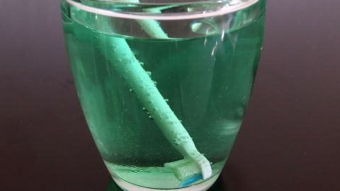 Eine elektrische Zahnbürste steht in einem Glas mit grünem Flüssigkeit, um sie schnell zu reinigen und sauber zu halten.
