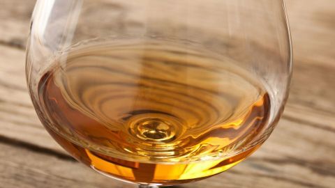 Ein Glas mit bernsteinfarbenem Getränk steht auf einer hölzernen Tischoberfläche und reflektiert das Licht.