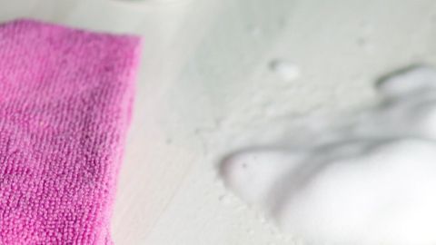 Ein pinkes Tuch liegt auf Laminat, daneben Schaum und eine Dose. Kontext: Reinigung von Laminat.