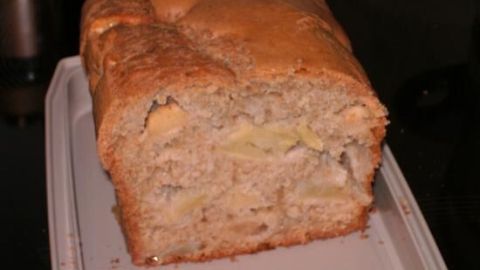 Ein goldbrauner Apfel-Selters-Kuchen liegt auf einem weißen Schneidebrett in einer dunklen Küche und sieht saftig aus.