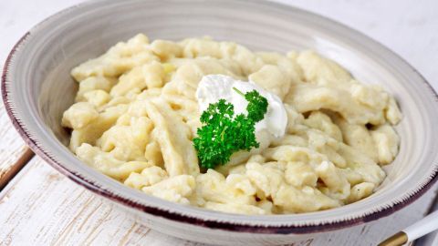 Ein Teller mit cremigem Kartoffelpüree, garniert mit einem Klecks Sahne und frischer Petersilie, steht auf einem Holzuntergrund.
