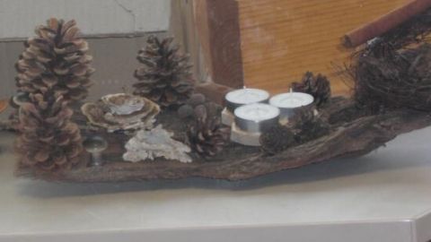 Eine dekorative Anordnung aus Naturmaterialien zeigt Zapfen und Kerzen auf einem Holzstück, ideal für weihnachtliche Deko.