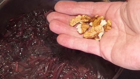Eine Hand streut gehackte Walnüsse über den köchelnden Rotkohl, der in einem Topf zubereitet wird.