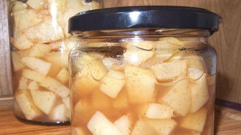 Glasbehälter mit stückigen, eingelegten Äpfeln in süßer Flüssigkeit stehen auf einer Holzfläche, die Zucker ersetzen können.