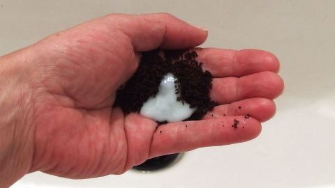 Eine Hand hält eine Mischung aus schwarzem Material und weißem Schaum, um Hände von Baumharz zu befreien.