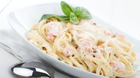 Eine Portion Spaghetti mit Lachs-Sahne-Soße liegt appetitlich in einer weißen Schale, garniert mit frischem Basilikum.