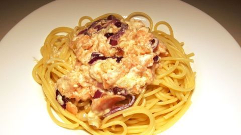 Spaghetti liegen auf einem Teller, umhüllt von einer cremigen Sauce mit Räucherlachs und weiteren Zutaten in einer schlichten Umgebung.
