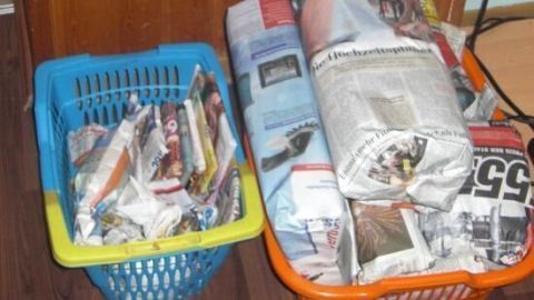 Körbe gefüllt mit in Zeitungspapier eingepackten Geschenken stehen auf einem Holzboden vor einer Holzwand.