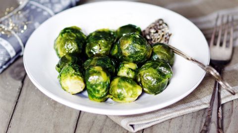 Köstlicher Rosenkohl liegt auf einem weißen Teller, umgeben von einem eleganten Besteck, bereit als Beilage zu Fleischgerichten.