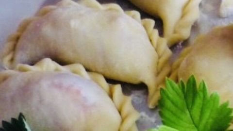 Leckere Pierogi z Kapusta i Grzybami liegen auf einem Teller, umgeben von frischen Blättern, bereit zum Servieren.