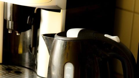 Ein Wasserkocher steht auf der Arbeitsfläche und wird zum Entkalken vorbereitet, während eine Kaffeemaschine im Hintergrund steht.