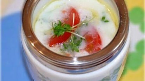 Ein Egg-Coddler enthält ein Eierrezept mit Tomaten und Kräutern, hübsch präsentiert auf einem bunten Untergrund.