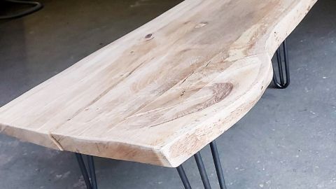 Ein Holztisch steht auf dünnen Metallbeinen in einer Garage, umgeben von Werkzeugen und Fahrrädern.