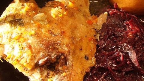 Ein gebratenes Gänsekeule, knusprig und goldbraun, liegt neben Rotkohl und einer Beilage in einem festlichen Ambiente.