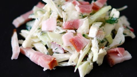 Warmer Krautsalat mit Speckwürfeln wird auf einem dunklen Teller angerichtet, frisch zubereitet und appetitlich angerichtet.