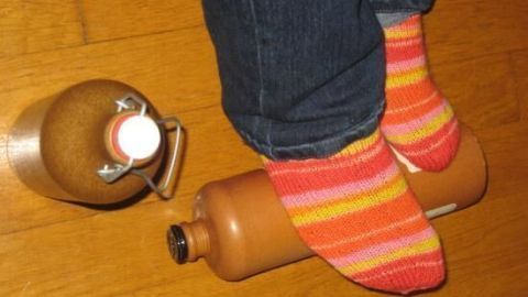 Wärmen mit einer Tonflasche, die unter bunten Socken steht, während eine zweite Flasche daneben liegt.