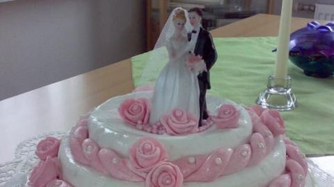 Eine mehrstöckige Hochzeitstorte mit rosa Rosen, garniert und mit Brautpaarfigur dekoriert, steht auf einem Tisch.