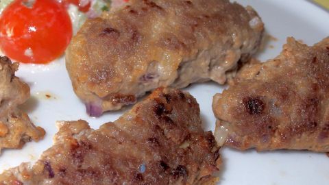 Cevapcici aus Fleisch vom Rind, vom Schwein und vom Schaf. Gegrillte Cevapcici liegen auf einem Teller neben einer bunten Gemüsemischung, bereit zum Servieren.