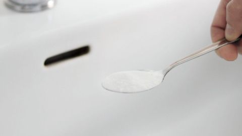 Ein Löffel mit Soda wird über einem verstopften Waschbecken gehalten, um die Verstopfung zu lösen.
