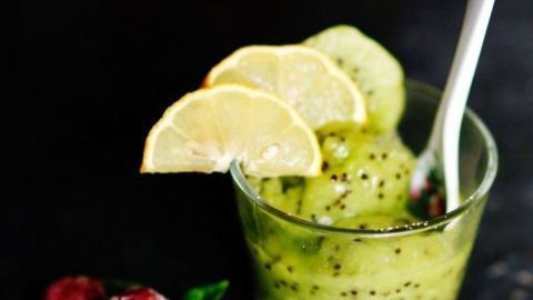 Ein Glas Kiwi-Limonen-Sorbet steht auf einem dunklen Hintergrund, dekoriert mit Zitronenscheiben und einer Löffel.