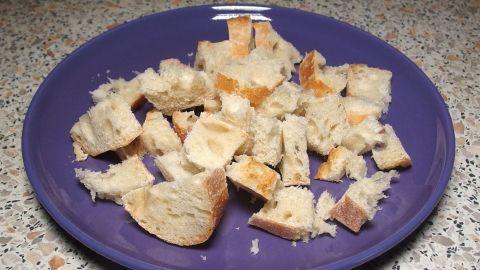 Auf einem lila Teller liegen Stücke von altbackenem Brot, die zum Verwenden in verschiedenen Gerichten vorbereitet sind.