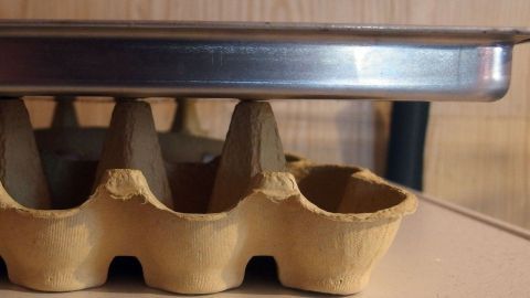 Zwei leere Eierkartons aus Pappe helfen beim Auskühlen von Plätzchen auf dem Backblech. Ein Backblech wird auf einem Papp-Eierkarton abgestellt, um Plätzchen auskühlen zu lassen, ohne einen speziellen Rost zu nutzen.