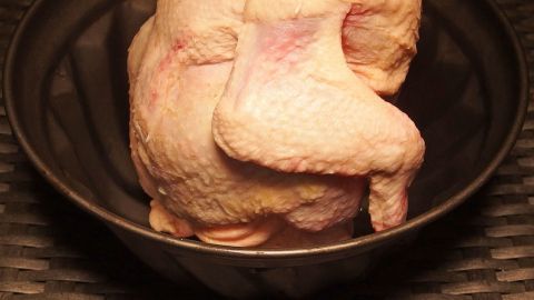 Ein ganzes Huhn liegt in einer Gugelhupfform, bereit zum Braten, auf einem gewebten Untergrund.