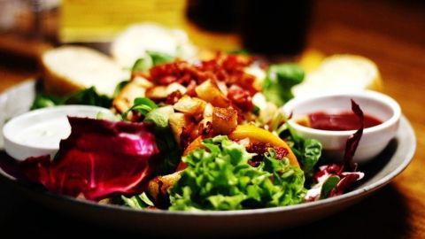 Ein Salat mit buntem Gemüse und zwei Saucen wird appetitlich auf einem Teller serviert, umgeben von Brotstücken.
