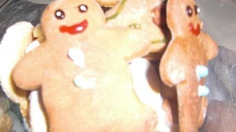 Lebkuchenmännel liegen in einer Glasschüssel, lächelnd und dekoriert, umgeben von mehr Lebkuchen und Süßigkeiten.