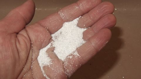 Weiße Spülmaschinenreiniger-Pulver liegt in einer Hand, bereit für die Reinigung fett-/ölverschmutzter Hände in der Küche.