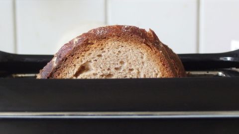 Ein Toastbrot steht aufrecht im Toaster und wird leicht geröstet, während helle Fliesen im Hintergrund sichtbar sind.