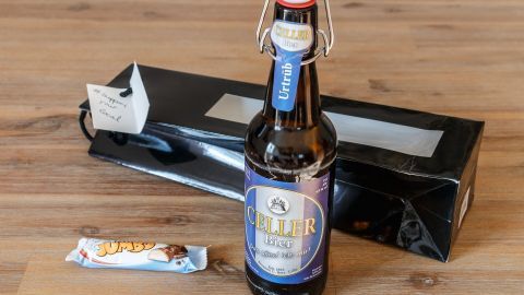 Ein dekorativ verpackter Adventskalender für Männer liegt neben einer Flasche Bier und einem Schokoriegel auf einem Tisch.