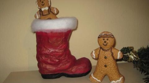 Ein roter Nikolausstiefel steht auf einem Tisch, gefüllt mit einem Lebkuchenmann, während ein weiterer daneben sitzt.